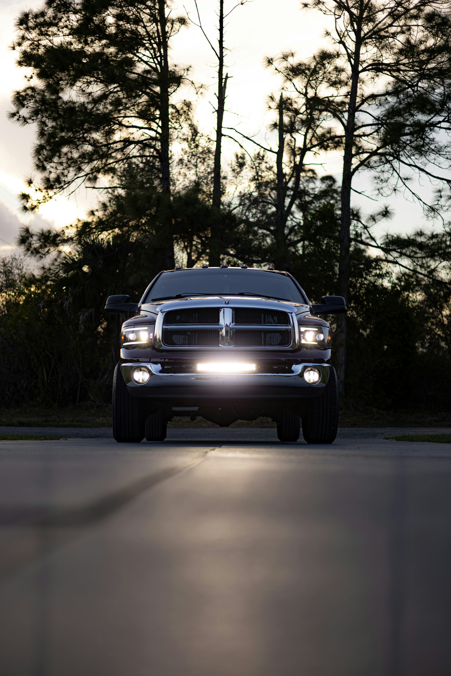 Dark pickup truck facing forward with its headlights illuminated