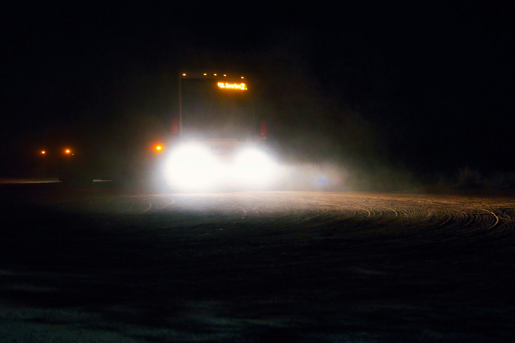 Truck headlights cutting through a dark road at night